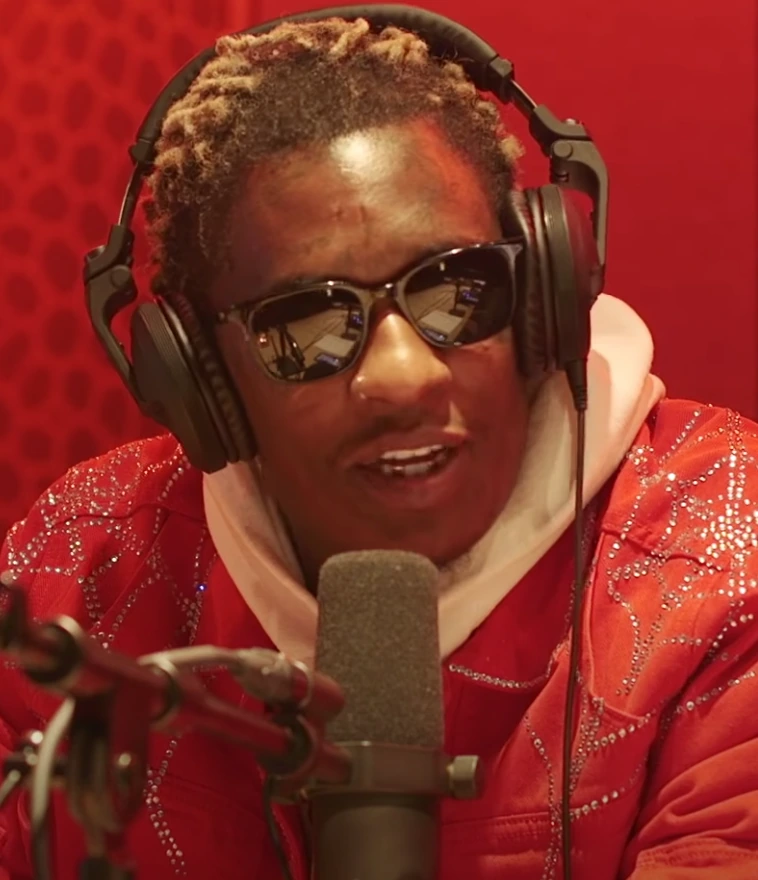 Young Thug in a red studio setting wearing sunglasses and headphones