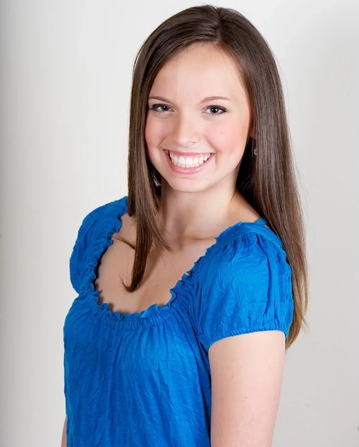 Portrait photo of Payton Alexandra Ackerman smiling in a blue top against a plain background.